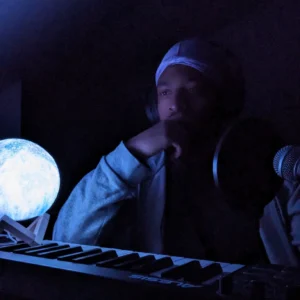 Rapper Zander, an American sitting in the dark with a midi keyboard in front of him and a spherical desk light to his right in the cover art for the 2024 single "In Your Dreams"