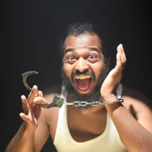 Rapper Zander, an American with a manic expression on his face displaying a set of handcuffs unlocked from one wrist as cover art for the single "Safe?"