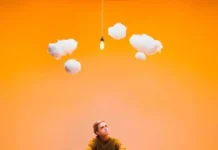 Devin Kennedy’s ‘Imagination’ Lands on Demure, Tuneful Ground Indie singer-songwriter Devin Kennedy sitting beneath small, playful white clouds with an orange background as part of marketing material for his album "In My Imagination"