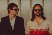 Brighton Duo Elandra Tear It All Apart in New Single “Ask Me Why” Brighton psychedelic pop-rock duo Elandra. (Left to right) bassist/co-producer George Seymour-Cole in a black blazer and shades; lead singer and co-producer Paolo Siviero in shades with shoulder-length brown hair and a patterned short-sleeved button-up shirt