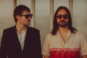 Brighton psychedelic pop-rock duo Elandra. (Left to right) bassist/co-producer George Seymour-Cole in a black blazer and shades; lead singer and co-producer Paolo Siviero in shades with shoulder-length brown hair and a patterned short-sleeved button-up shirt