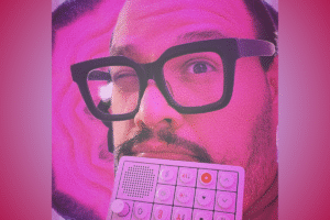 Frank Panduh pictured with thick-framed glasses holding a white music production pad with a gradient pink backdrop; feature photo for a review of his single "Cabbage"